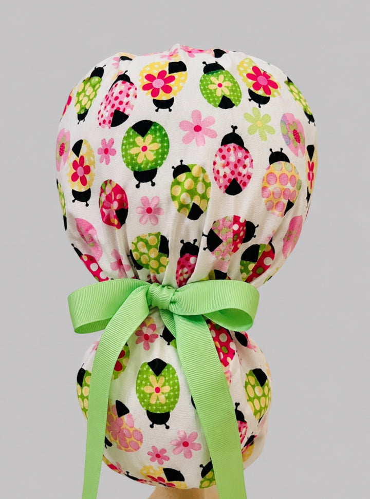 Ladybug daisy ponytail scrub cap back view close-up showing gathered pouch full of colorful floral ladybugs, daisies and green ribbon bow