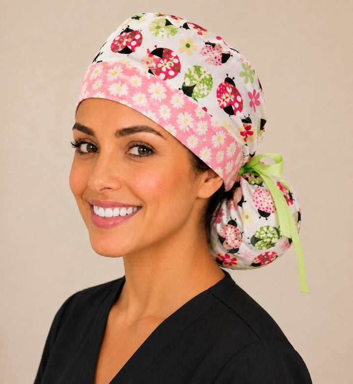 Ladybug daisy ponytail scrub cap left three-quarter angle showing full ponytail pouch of floral ladybugs and daisies with green ribbon bow