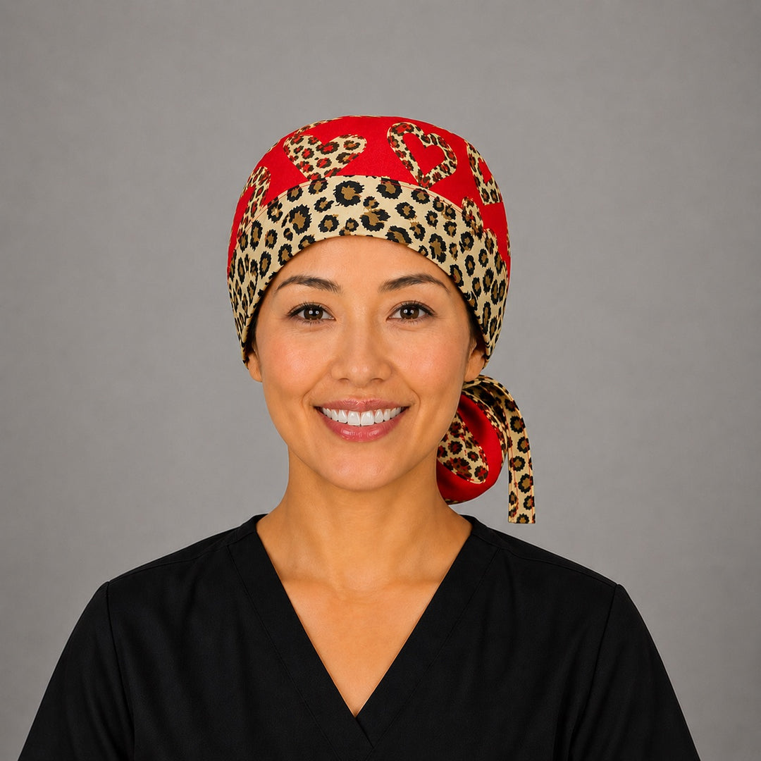 Woman wearing leopard print hearts ponytail scrub cap, front view smiling with leopard-print hearts on red and cheetah-print band with animal-print ribbon tie