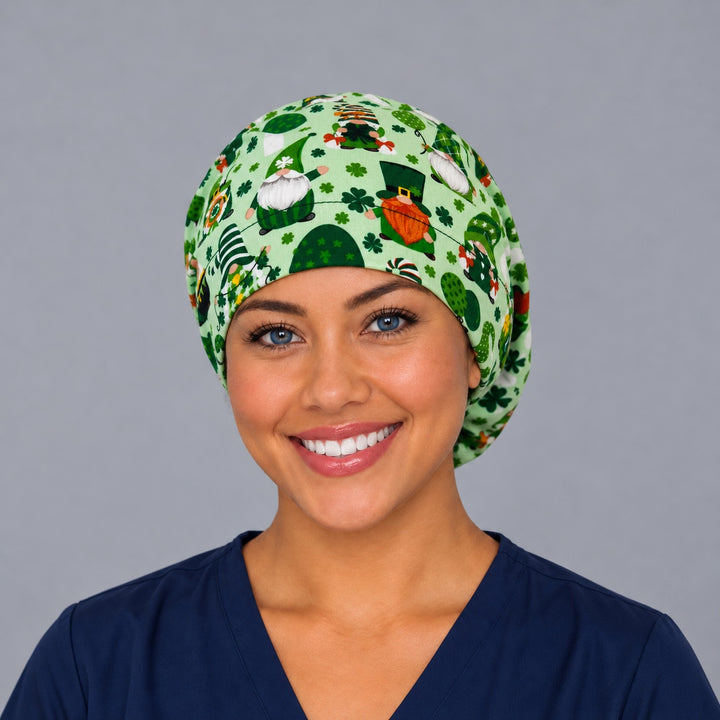 Woman wearing a leprechaun gnome Euro scrub cap, front view — shamrocks and gnomes on mint green, adjustable St. Patrick&