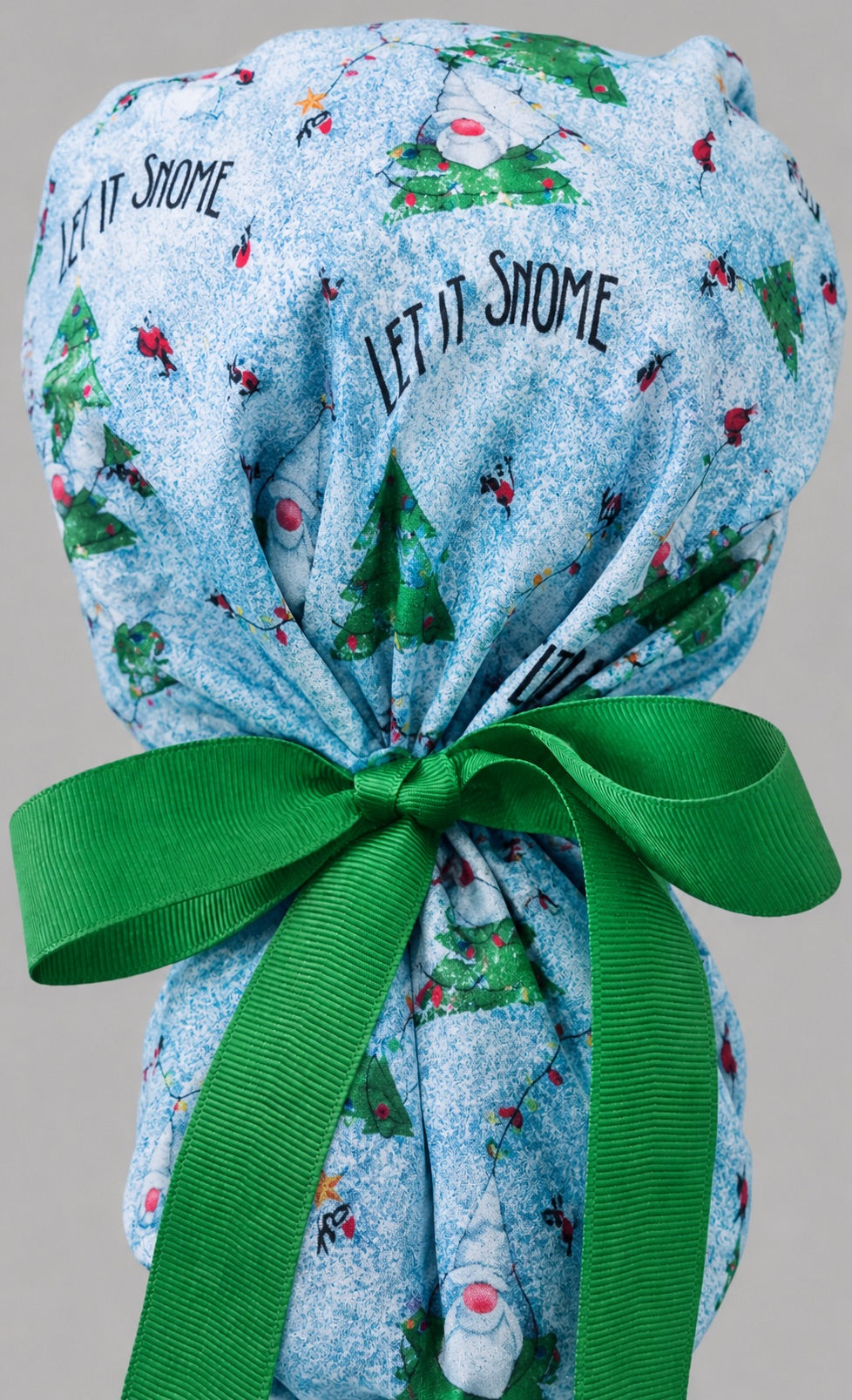 Let it Snome Christmas gnomes ponytail nurse cap left three-quarter angle on smiling model showing tree-gnomes, cardinals and green snowball band with green ribbon bow