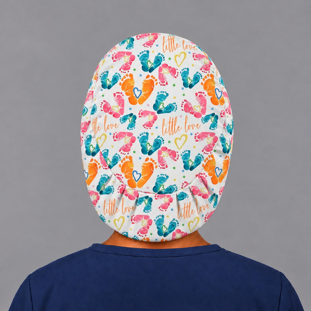 Back view of the Little Love euro scrub cap, showing the oval crown panel of baby footprints and the evenly pleated elastic band at the nape