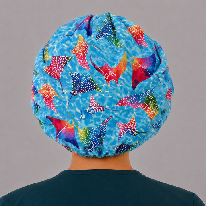 Back view of the colorful manta ray bouffant scrub cap — full roomy fit showing rainbow stingrays gliding across a bright ocean-blue print