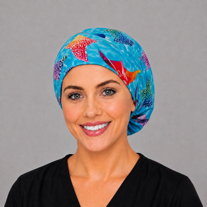 Woman wearing a manta ray Euro scrub cap, front view — colorful batik stingrays on turquoise water, adjustable surgical hat