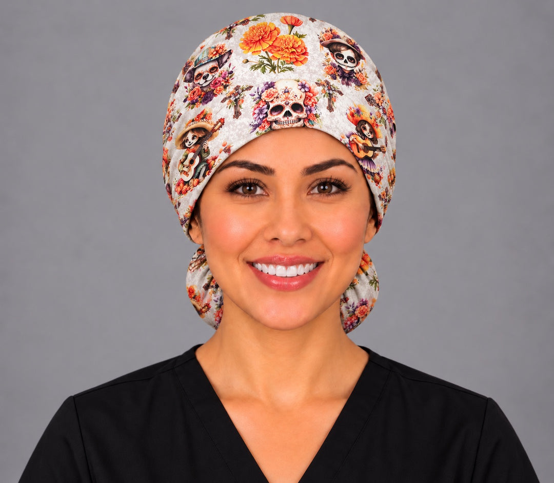 Front view of a nurse wearing the Mexican marigold ponytail scrub cap, flower crowned sugar skull above the brow and the hair pouch peeking out behind