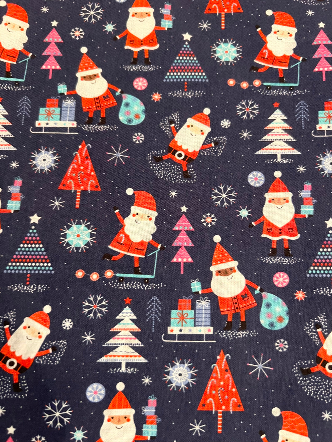 Christmas Santa ponytail scrub cap featuring cheerful Santas, Christmas trees, presents, candy canes, snowflakes, and festive holiday designs on a navy blue background, handmade surgical cap for nurses, surgeons, dental professionals, veterinarians, and healthcare workers, fabric view