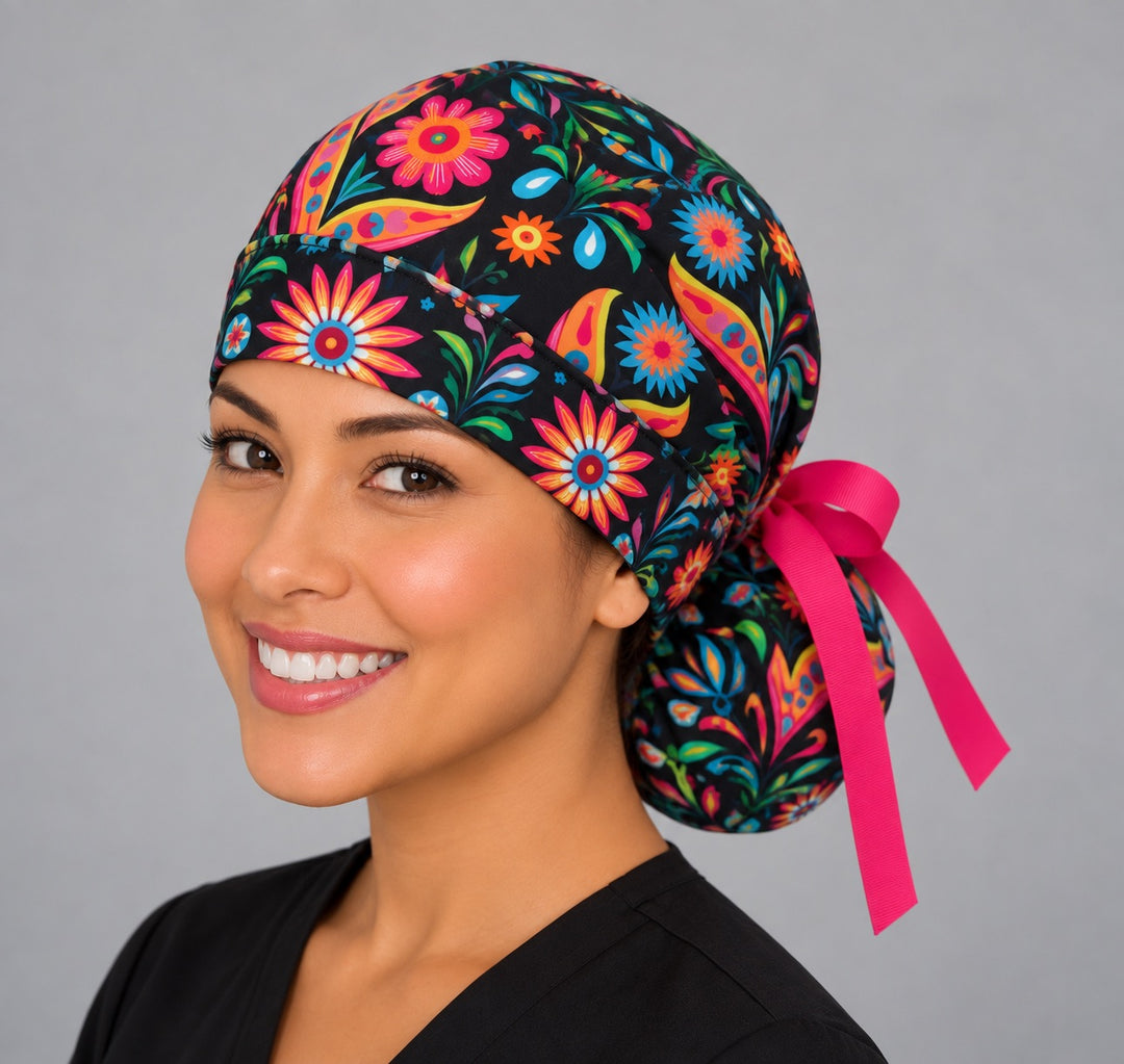Back view of the Mexican floral ponytail scrub cap — hot pink grosgrain bow tied over the pouch with folk-art flowers on black