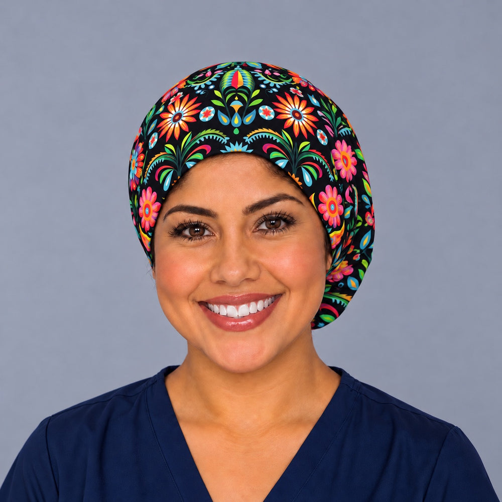Smiling nurse in navy scrubs wearing a Mexican floral euro scrub cap, front view of the black folk flower band with orange sunbursts centered above the forehead