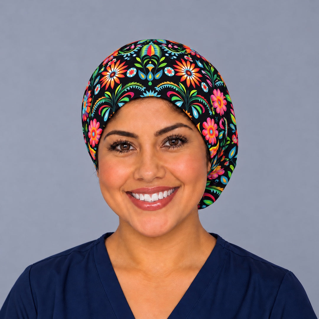 Smiling nurse in navy scrubs wearing a Mexican floral euro scrub cap, front view of the black folk flower band with orange sunbursts centered above the forehead