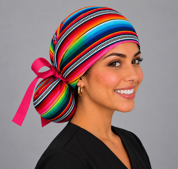 Smiling Latina nurse in a Mexican serape ponytail scrub cap with rainbow sarape stripes and hot pink bow
