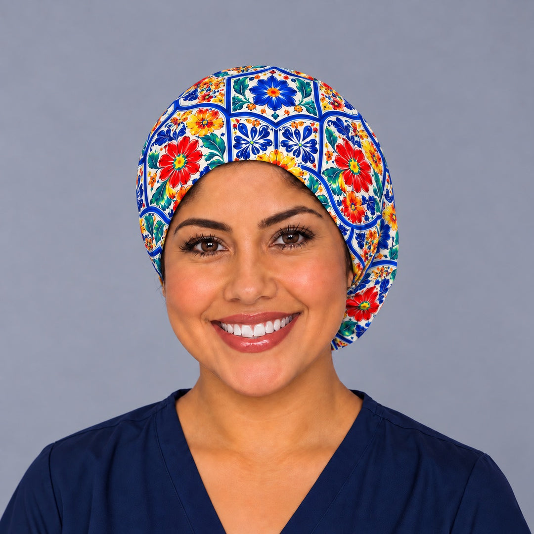 Smiling nurse in navy scrubs wearing a Mexican Talavera Euro scrub cap, front view of the elastic edge framing the hairline with cobalt tile panels across the crown