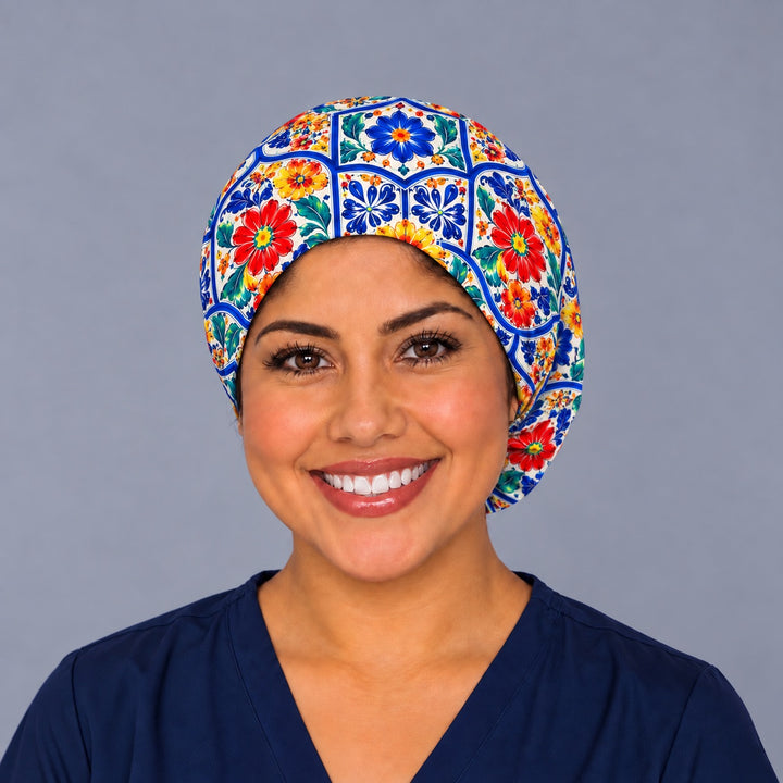 Smiling nurse in navy scrubs wearing a Mexican Talavera Euro scrub cap, front view of the elastic edge framing the hairline with cobalt tile panels across the crown