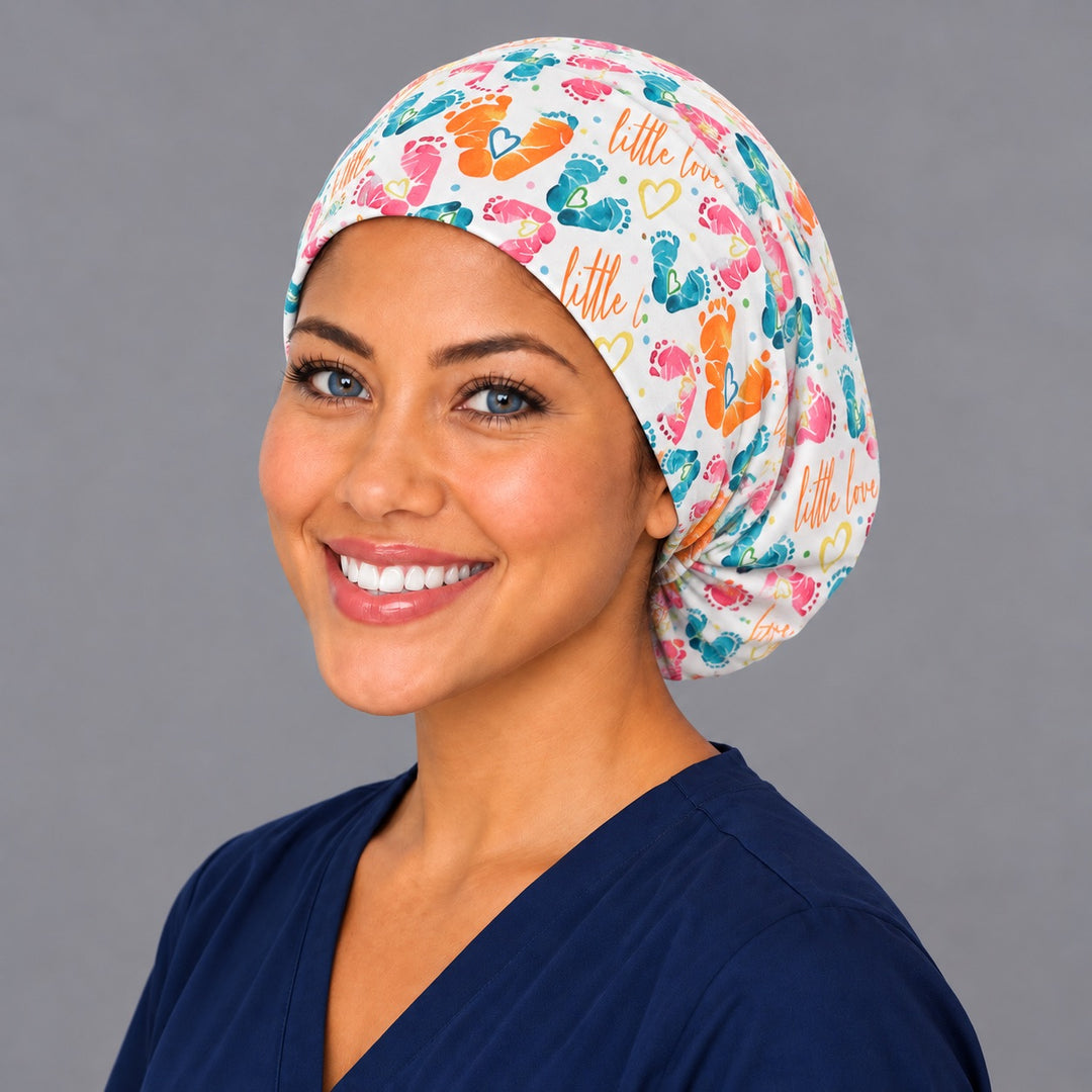 Left three-quarter angle of a smiling midwife in a baby feet scrub cap, with yellow outline hearts and rainbow dots at true print scale along the band