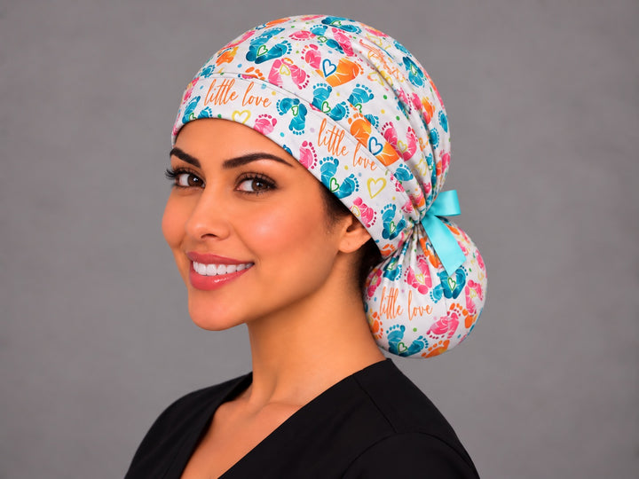 Left three-quarter angle of a smiling midwife in a ponytail scrub cap, with yellow outline hearts and confetti dots along the band at true print scale