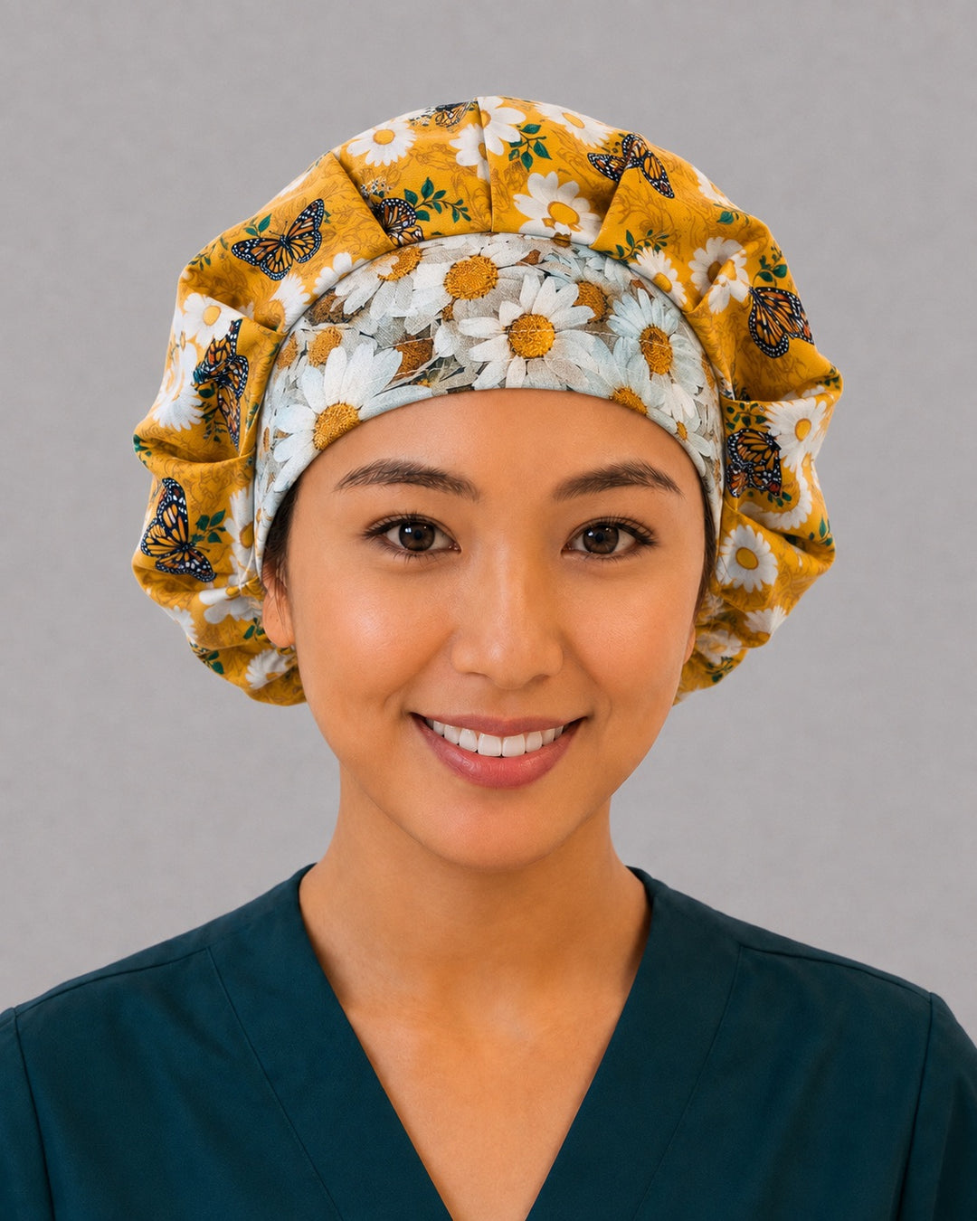 Woman wearing a monarch butterfly bouffant scrub cap, front view — mustard gold daisy print with orange monarchs and pale-blue daisy band, adjustable women&