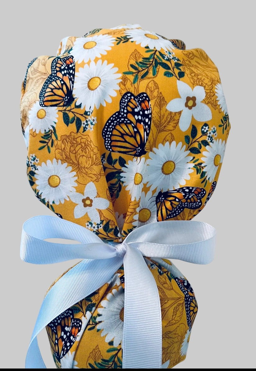 Monarch butterfly daisy ponytail scrub cap back view close-up showing gathered pouch full of orange monarchs, white daisies on golden yellow and white ribbon bow