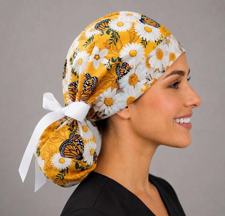 Woman wearing monarch butterfly daisy ponytail scrub cap, front view smiling with orange monarchs, white daisies on golden yellow with daisy band