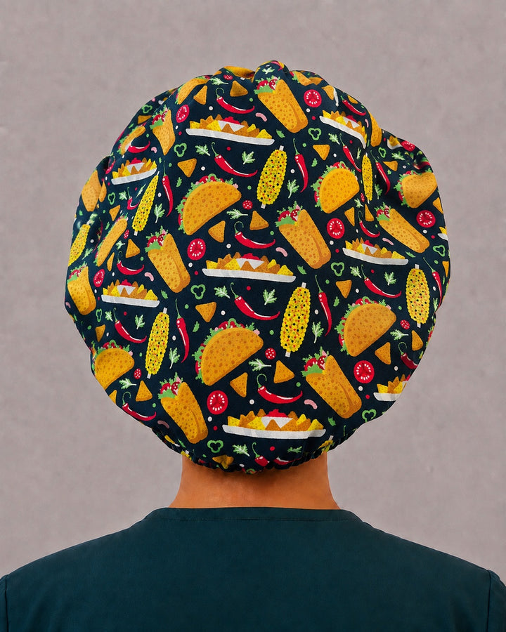 Woman wearing a Nacho Average Scrub Tech bouffant scrub cap, front view — taco print with gold embroidered band, adjustable women&