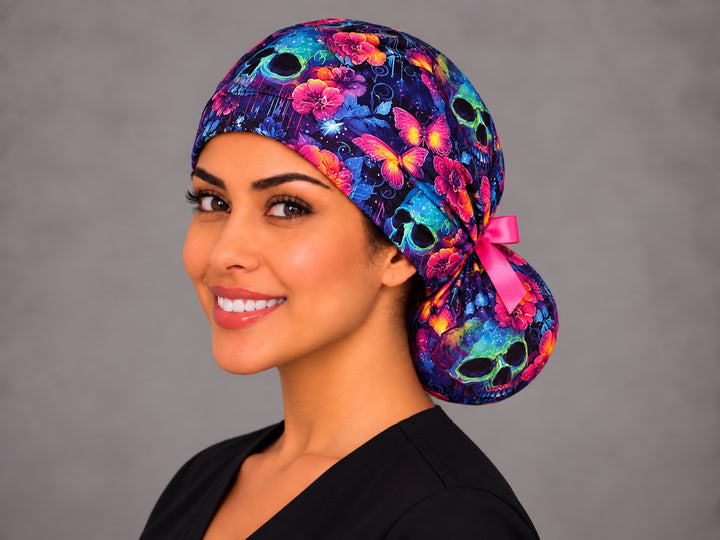 Neon calavera ponytail scrub cap, left three-quarter view, Mexican Día de los Muertos surgical hat for long hair with hot pink bow
