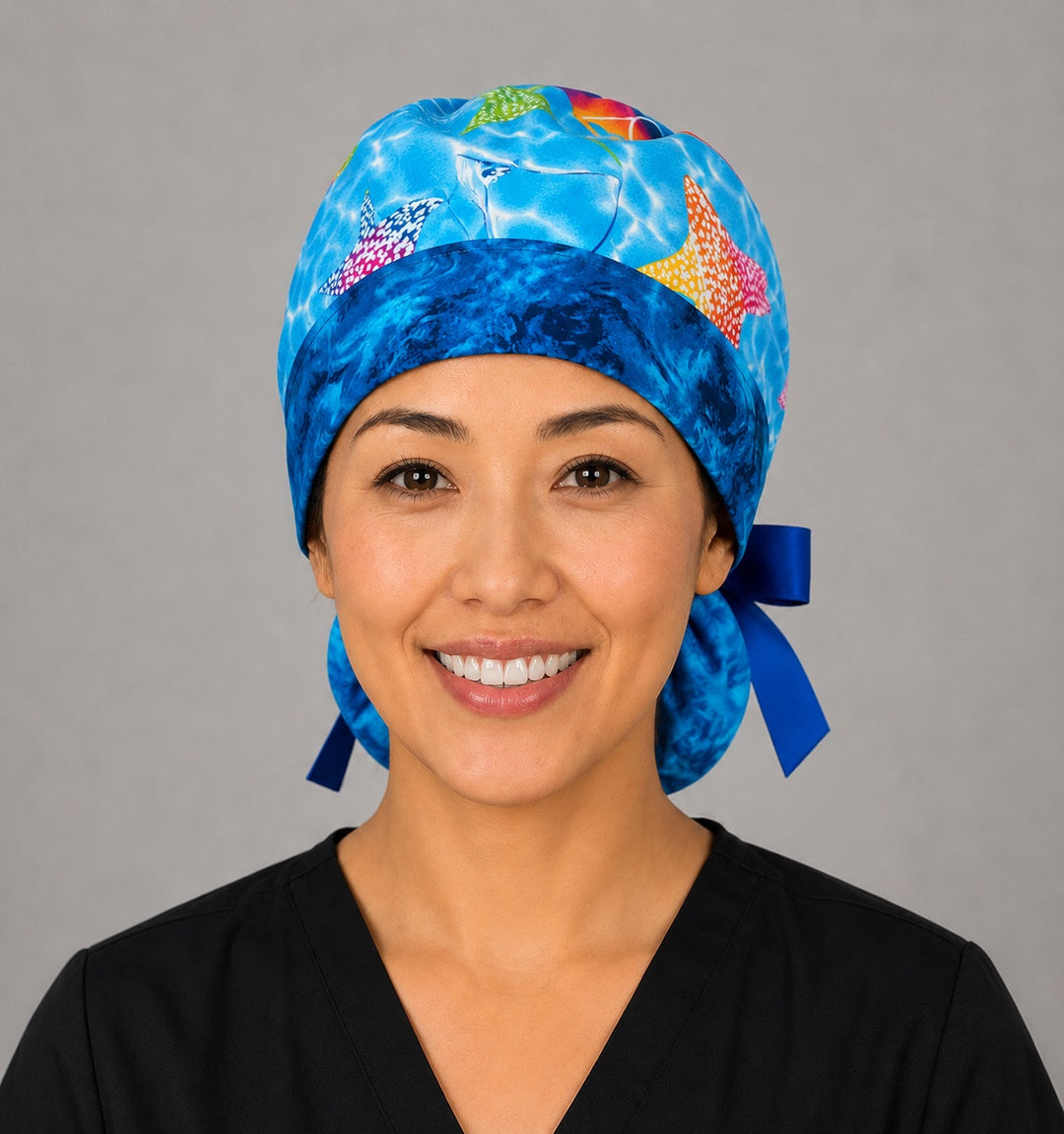 Woman wearing ocean stingray ponytail scrub cap, front view smiling with colorful rainbow stingrays on blue water and navy ribbon tie
