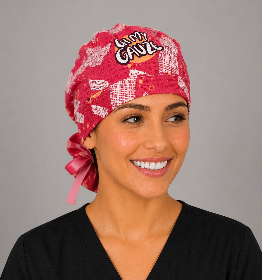 Woman wearing Oh My Gauze ponytail scrub cap, front view smiling with pink medical gauze print, funny Oh My Gauze text and pink ribbon tie