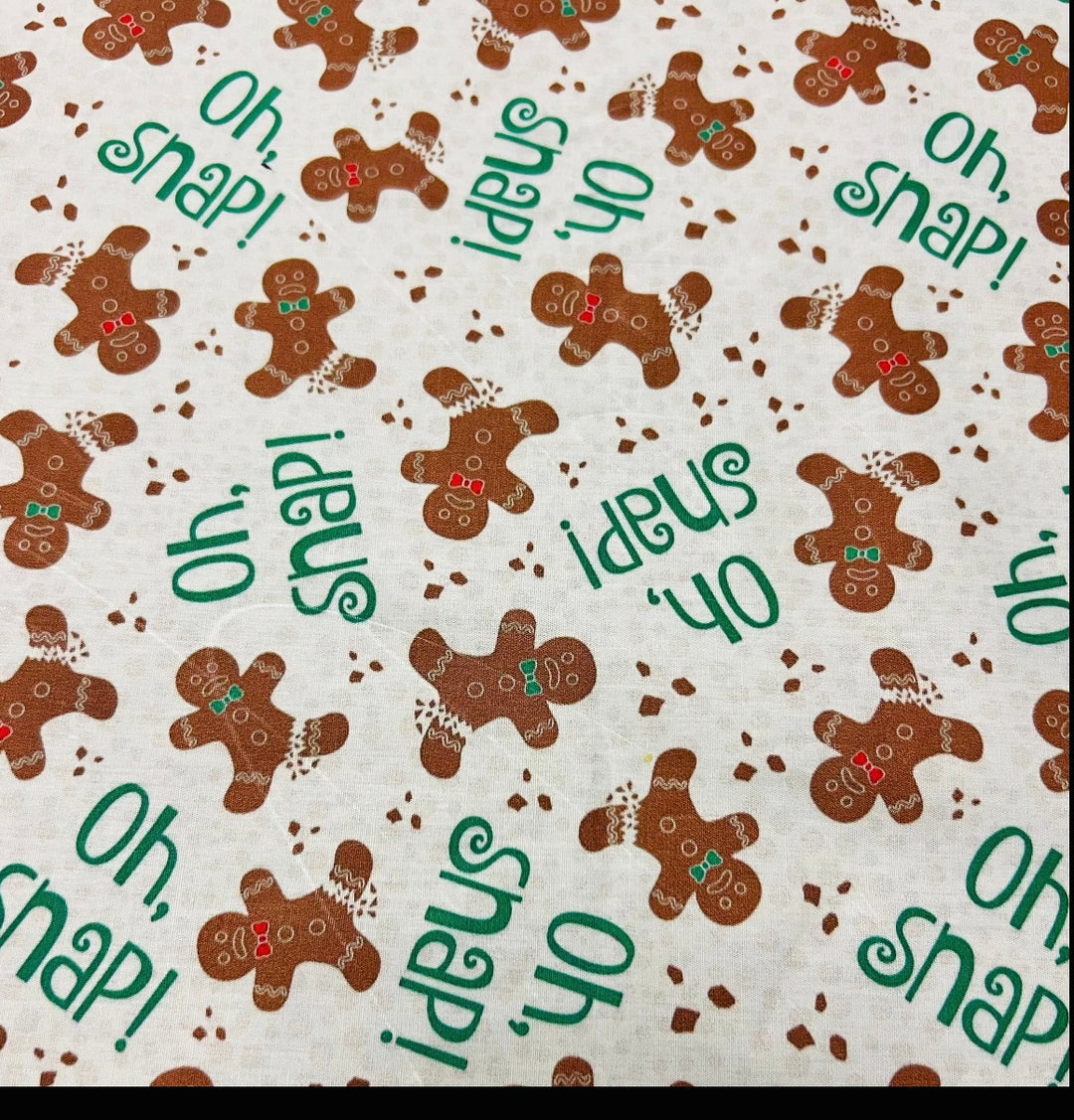 Fabric detail of the Oh Snap gingerbread scrub cap — close-up of gingerbread men with bow ties and green lettering on cream cotton