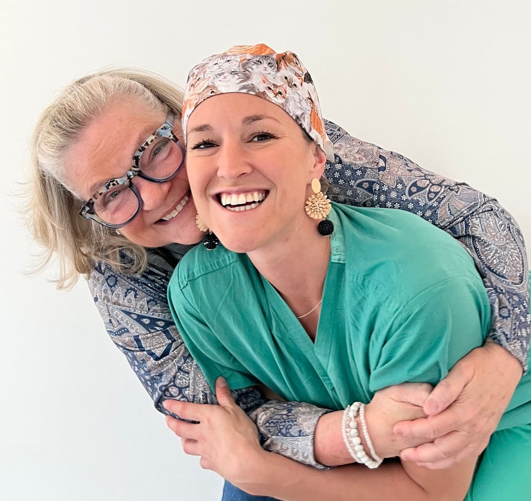 Mother and daughter cofounders of OR World Surgical Hats LLC sharing a hug, featuring Nancy Mamerow, seamstress and COO, and Sara Mamerow, former surgical tech and cofounder, celebrating their family-owned scrub cap business.