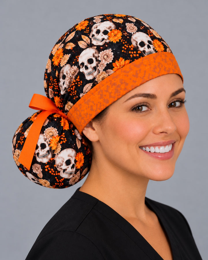 Three-quarter angle of an orange floral skull nurse cap, with ivory skulls and cream dahlias across the gathered crown on black cotton