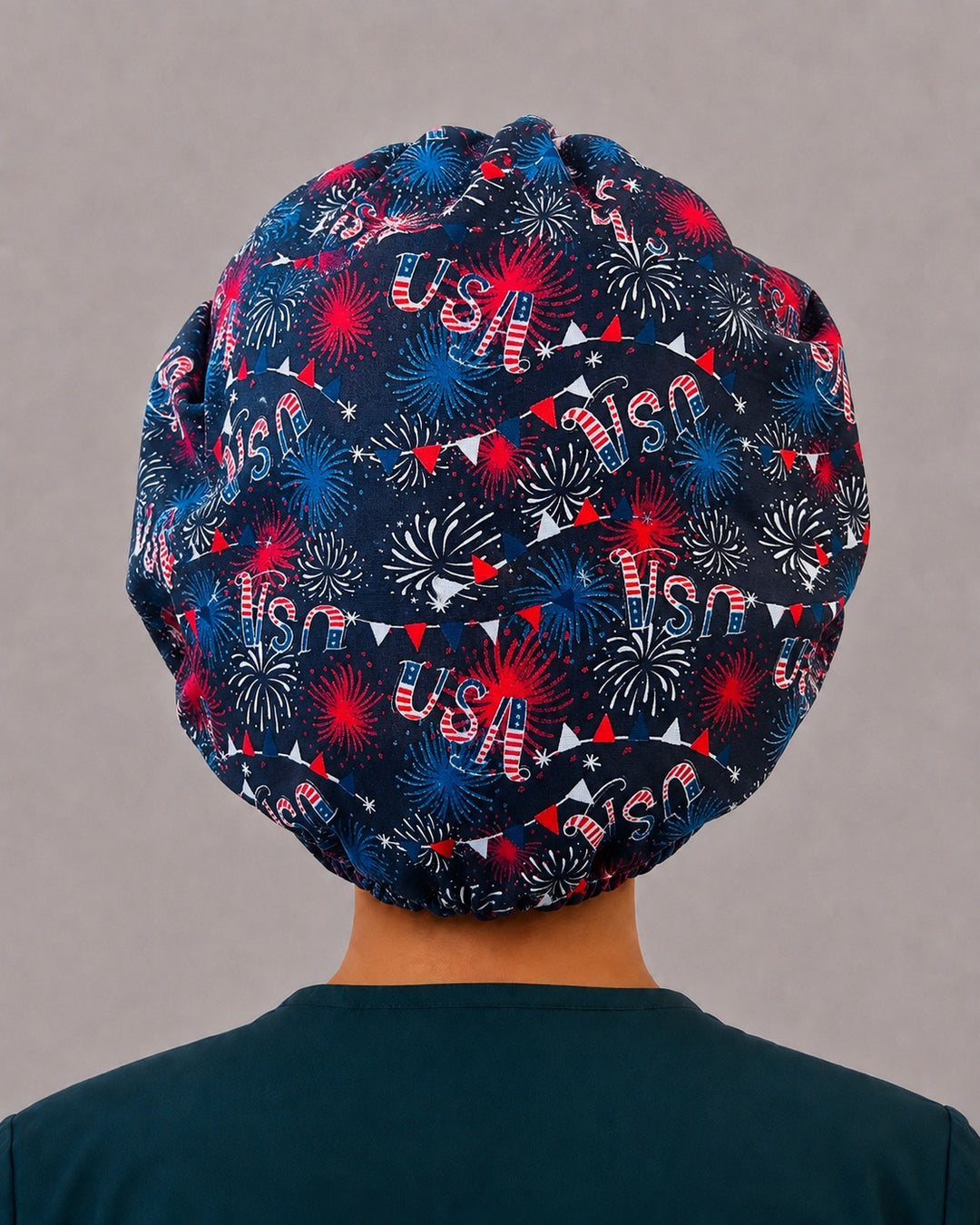 Woman wearing a patriotic fireworks bouffant scrub cap, front view — red, white and blue starbursts on navy with fireworks band, adjustable women&