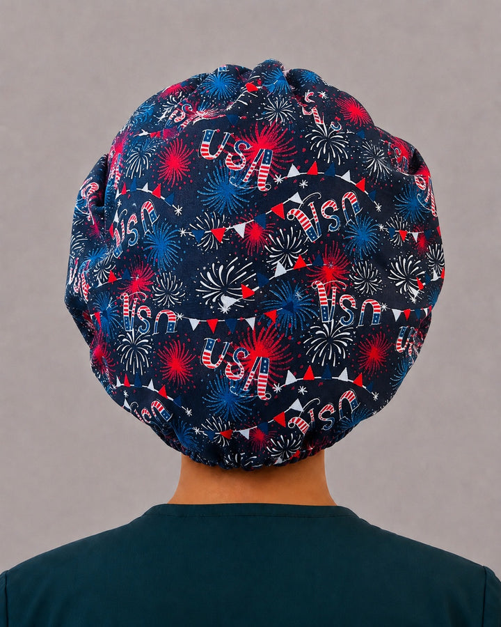 Woman wearing a patriotic fireworks bouffant scrub cap, front view — red, white and blue starbursts on navy with fireworks band, adjustable women&