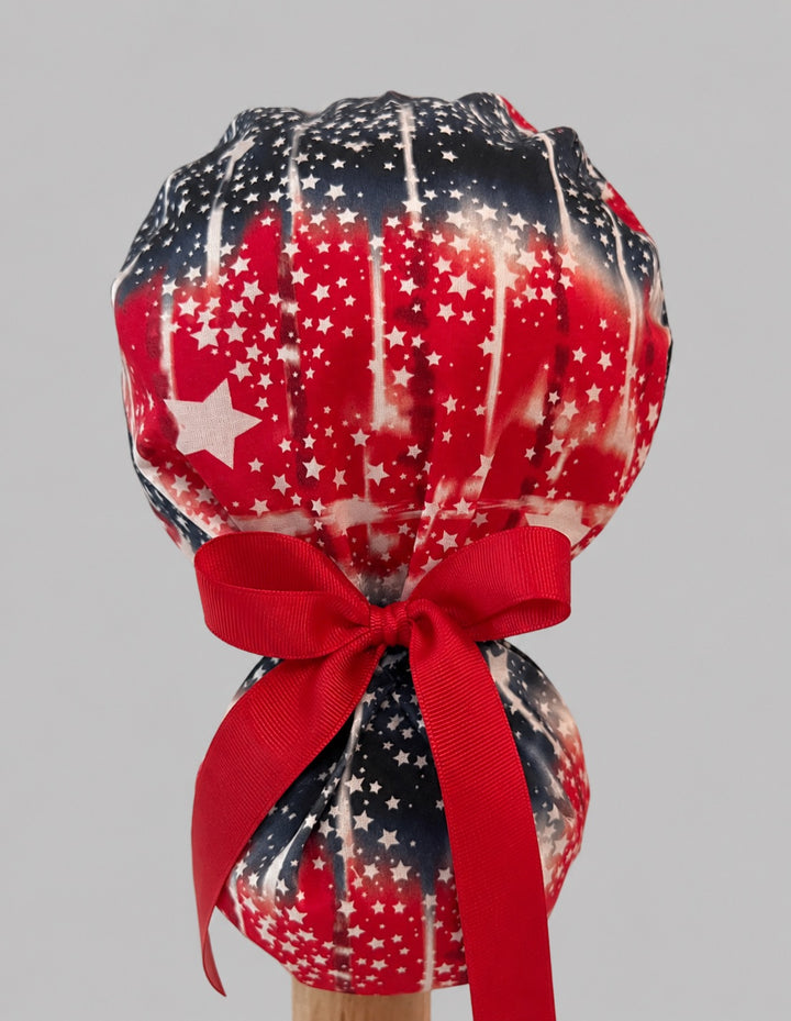 Back view of patriotic tie-dye ponytail scrub cap with red bow tie closure, American flag stars nurse hat, OR World