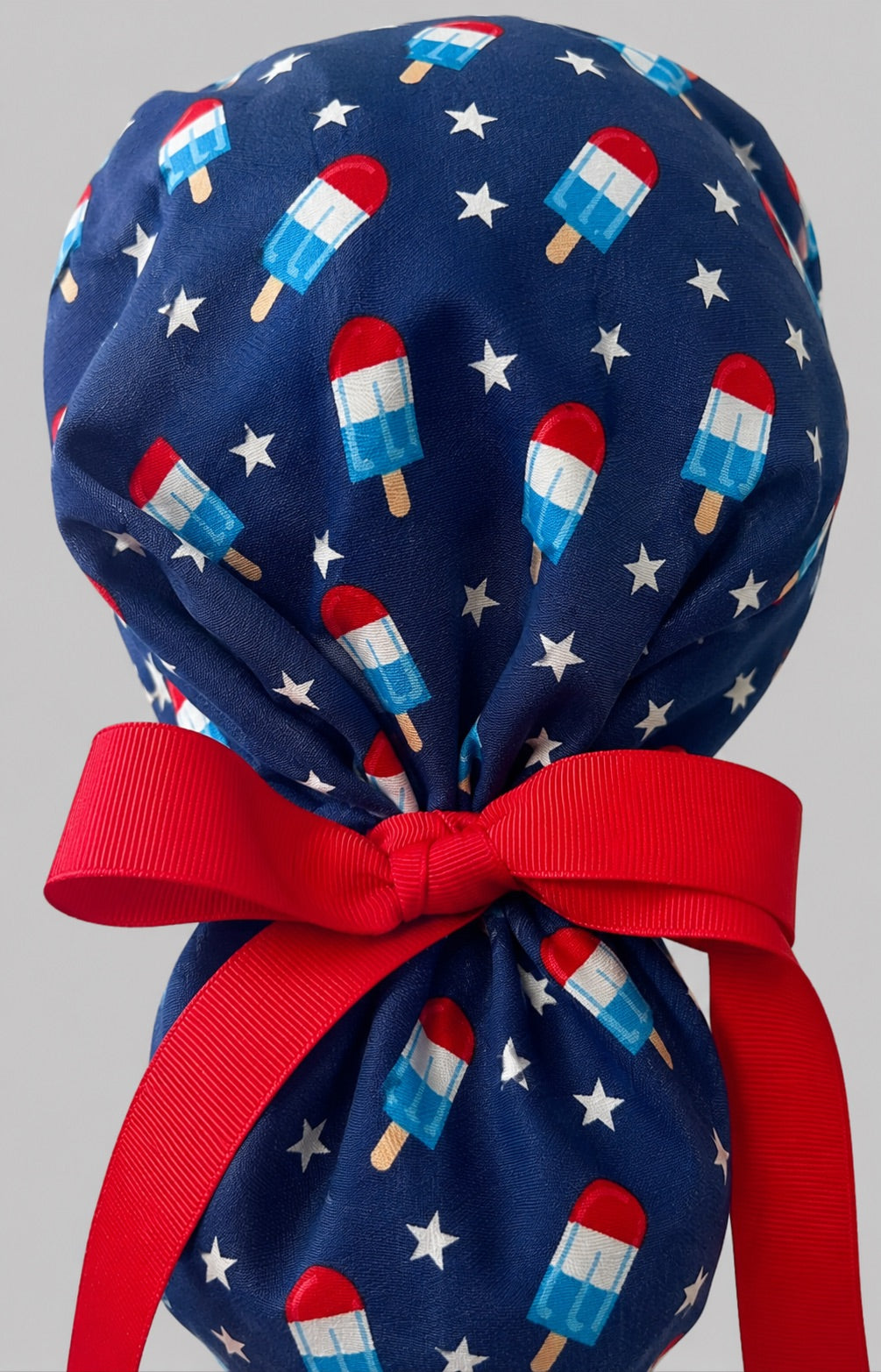 Patriotic popsicle ponytail scrub cap back view close-up showing gathered pouch full of red white blue popsicles, white stars and red ribbon bow