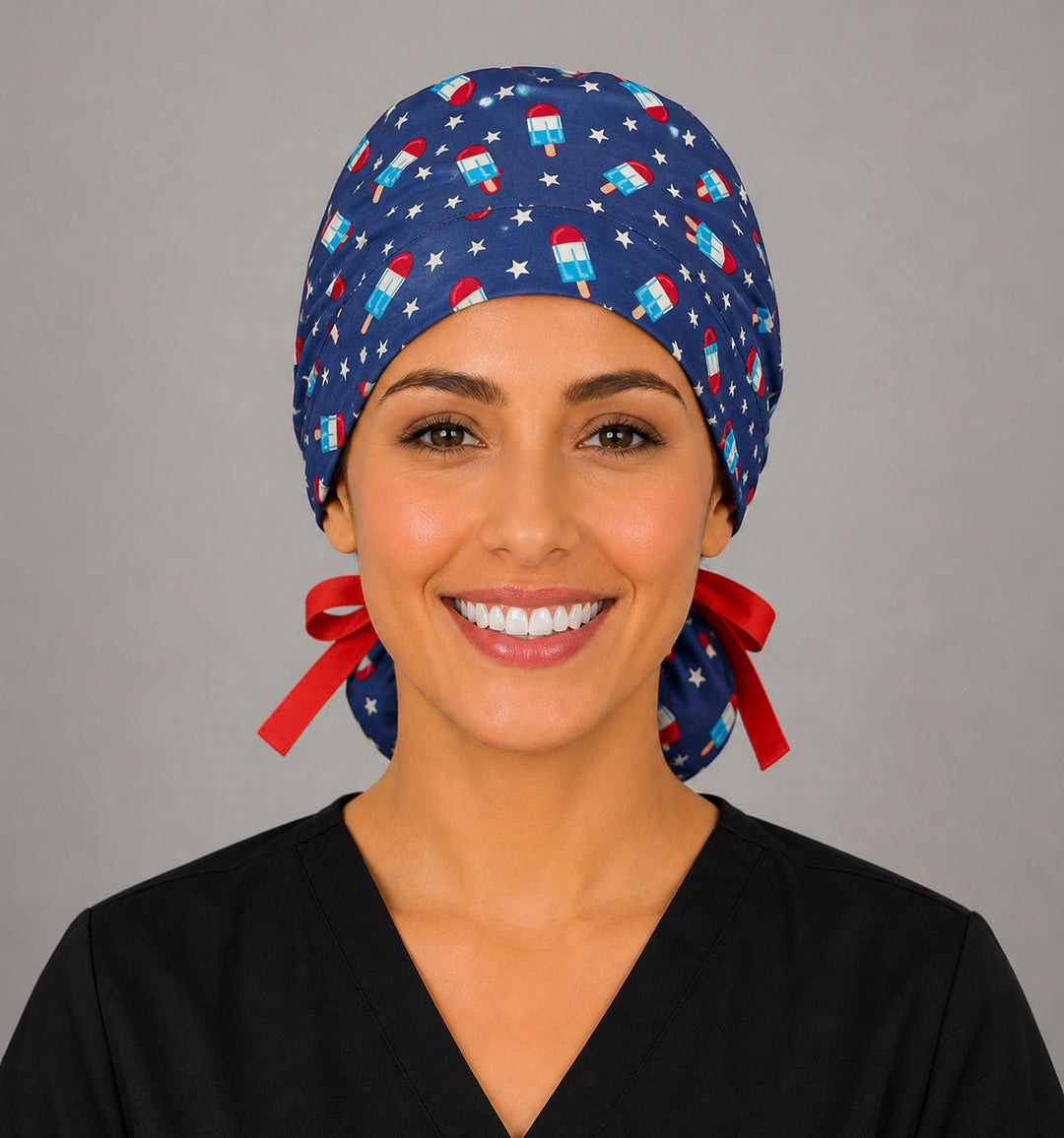 Woman wearing patriotic popsicle ponytail scrub cap, front view smiling with red white and blue popsicles and stars on navy and red ribbon tie