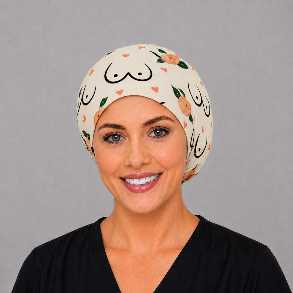 Woman wearing a Peaches of Hope Euro scrub cap, front view — breast anatomy line art with peaches and hearts on cream, adjustable surgical hat