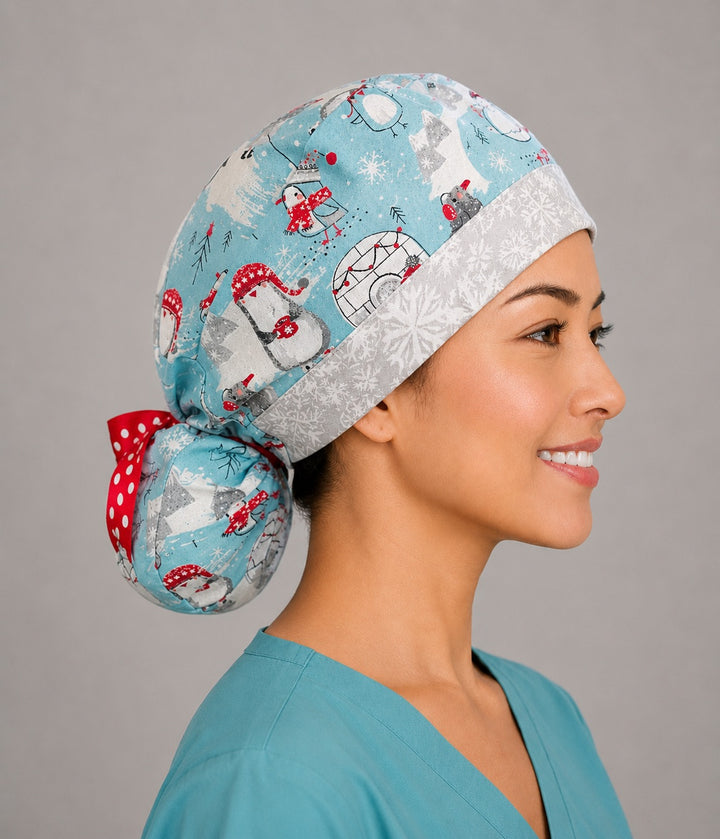 Penguins and igloos ponytail scrub cap back view close-up showing gathered pouch full of penguins in red scarves, igloos, polar bears and snowflakes on light blue with red polka-dot ribbon bow