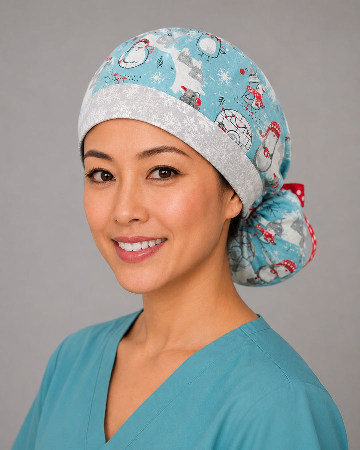Penguins and igloos ponytail scrub cap right side profile with full ponytail pouch of penguins, igloos and snowflakes on light blue and long red polka-dot ribbon ties