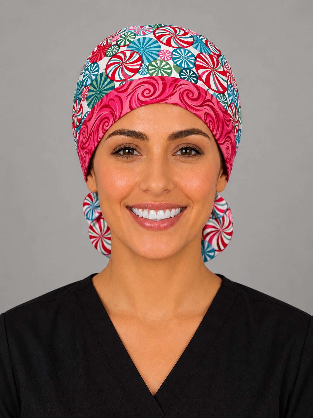 Woman wearing a peppermint swirl ponytail scrub cap, front view — red, teal and green candy swirls with a hot pink swirl band