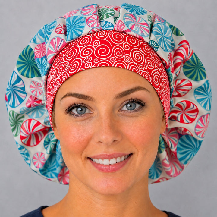 Woman wearing a peppermint swirl bouffant scrub cap, front view — red, teal and pink candy swirls with a red spiral band, adjustable women&