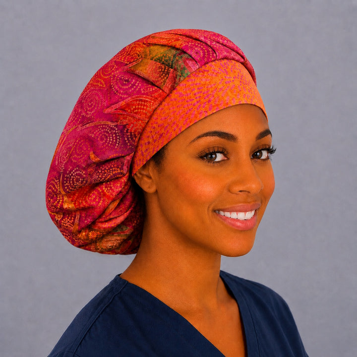 Pink and orange batik bouffant scrub cap, right angled smiling view — fuchsia swirl print with orange batik band, roomy adjustable surgical hat for women