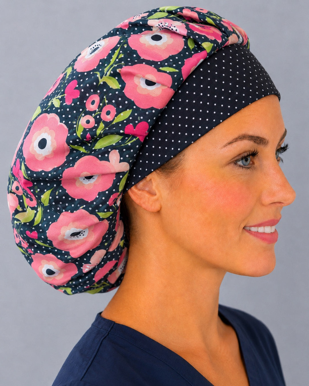 Woman wearing a pink poppy polka dot bouffant scrub cap, front view — pink florals on black with white dots, adjustable women&