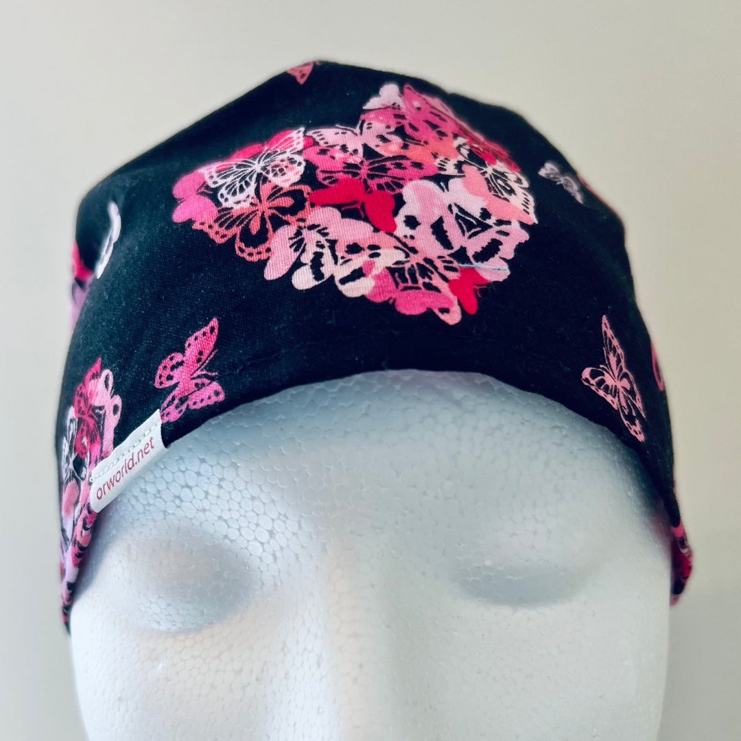 Front detail of pink ribbon and butterfly heart scrub cap on black, breast cancer awareness surgical hat