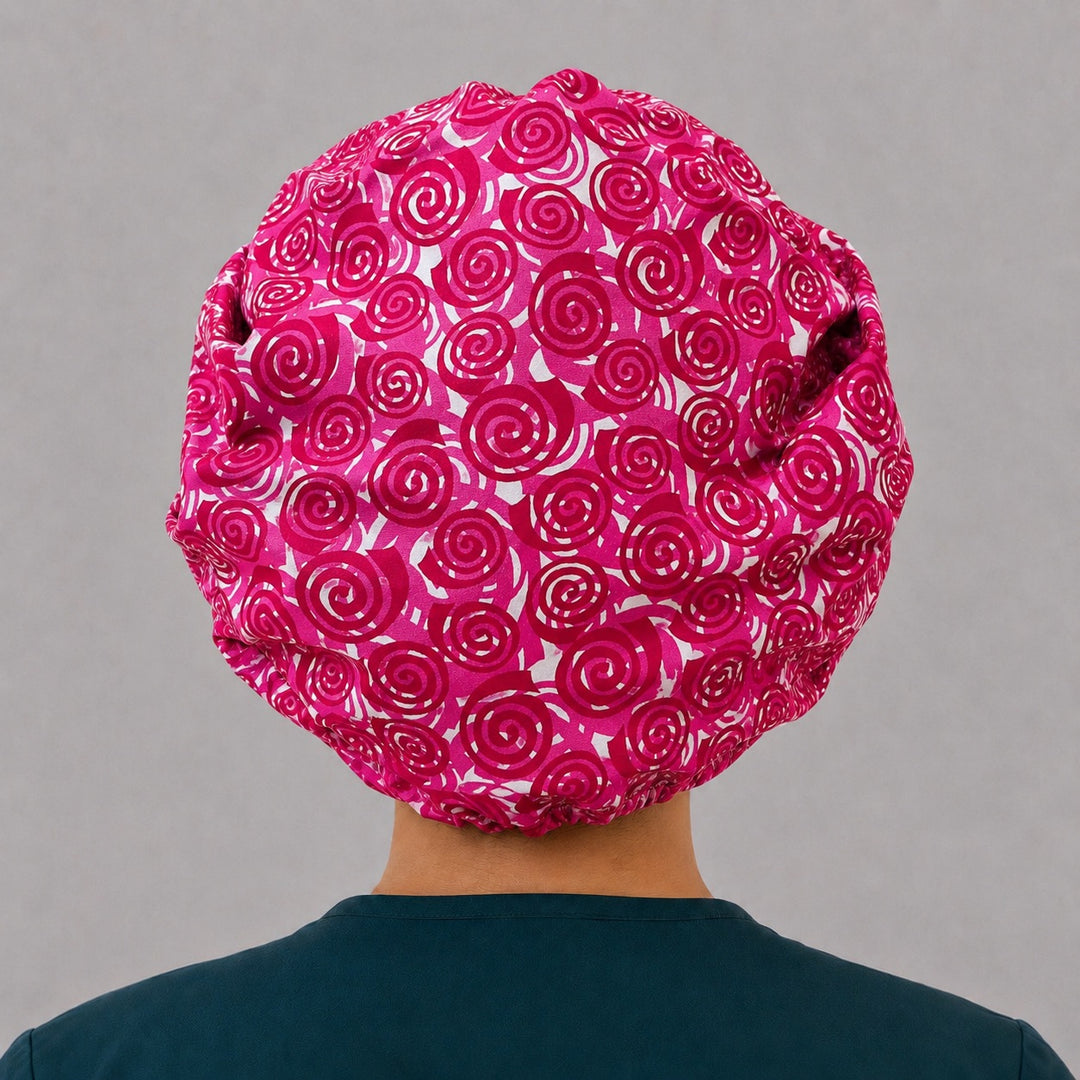 Woman wearing a pink swirl bouffant scrub cap, front view — hot pink and magenta spirals on white, adjustable women&