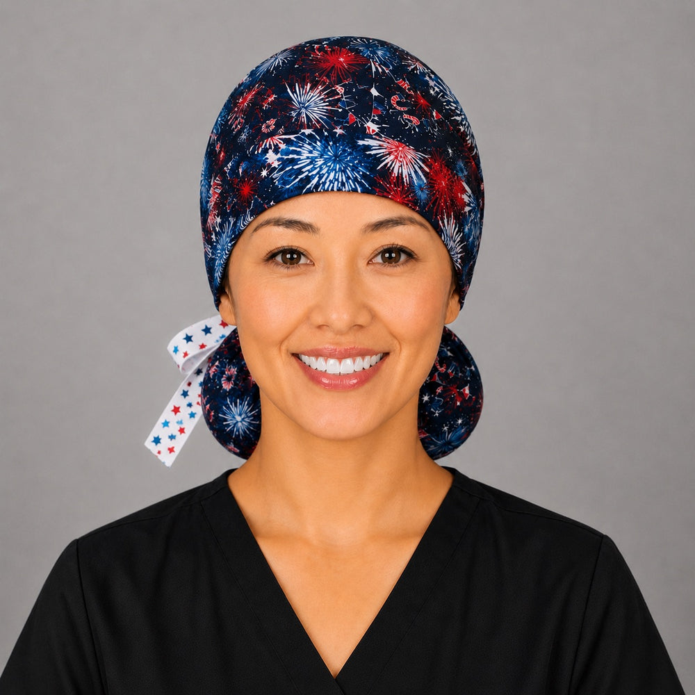 Front view of patriotic fireworks ponytail scrub cap for women in navy with red white and blue fireworks and star ribbon tie