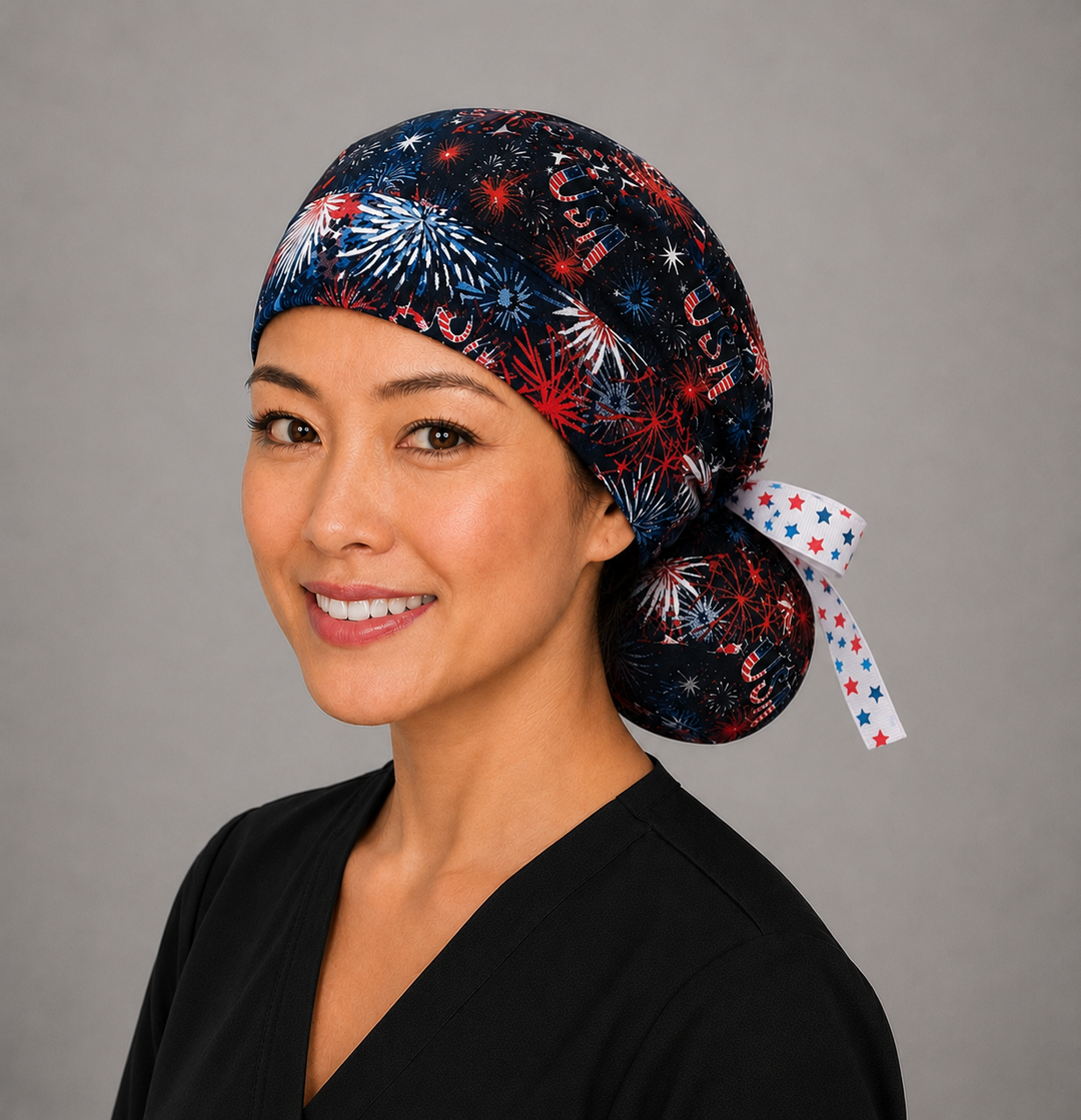Three-quarter view of patriotic USA fireworks ponytail surgical cap for women with ponytail pouch and star-print ribbon bow