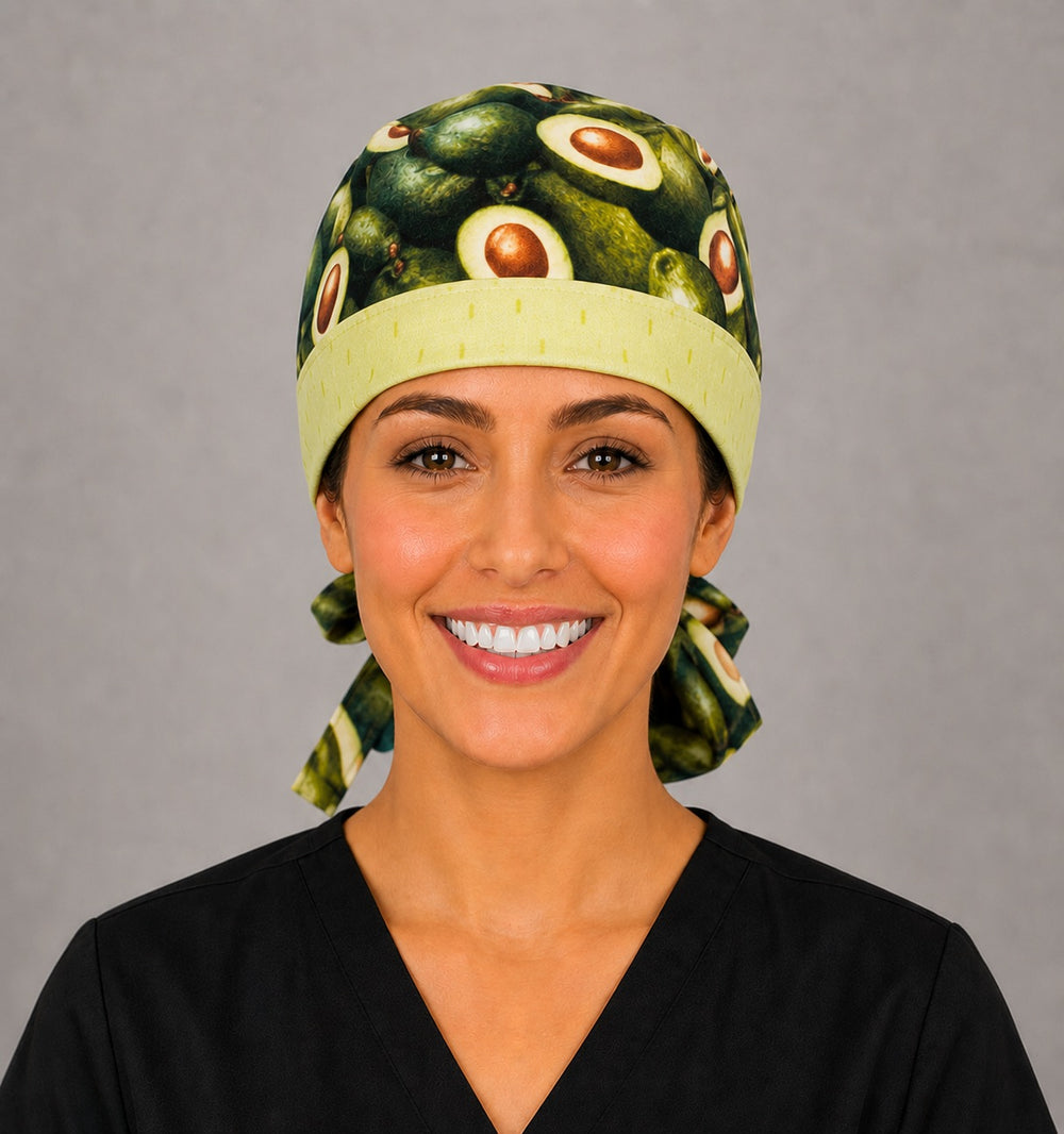Woman wearing avocado print ponytail scrub cap, front view smiling with light green band and whole and halved avocados