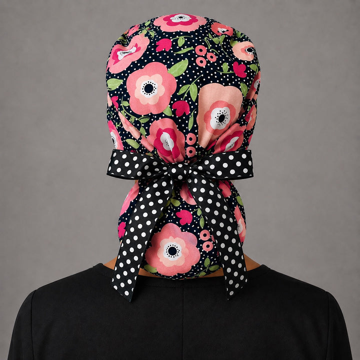 Black floral polka dot ponytail scrub cap back view on mannequin showing gathered pouch of pink poppies and black-and-white polka dot ribbon bow
