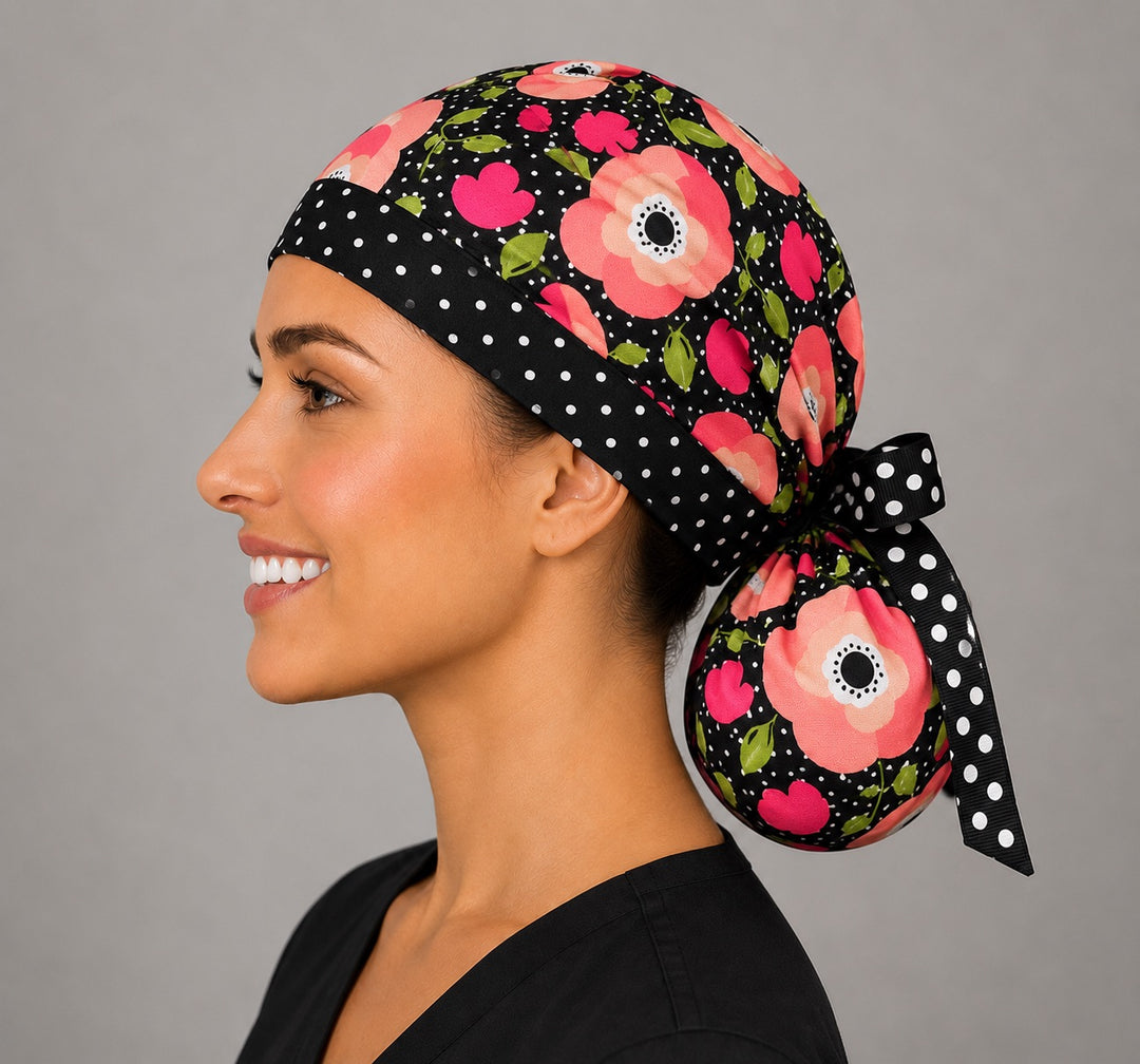 Woman wearing black floral polka dot ponytail scrub cap, left side profile with coral poppies and black-and-white polka dot ribbon bow