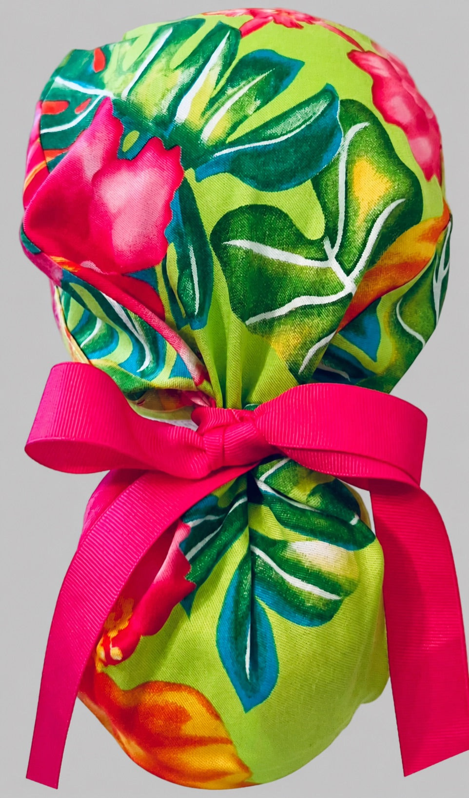 Hawaiian hibiscus tropical ponytail scrub cap back view on mannequin showing gathered pouch of pink and green tropical florals and hot pink ribbon bow