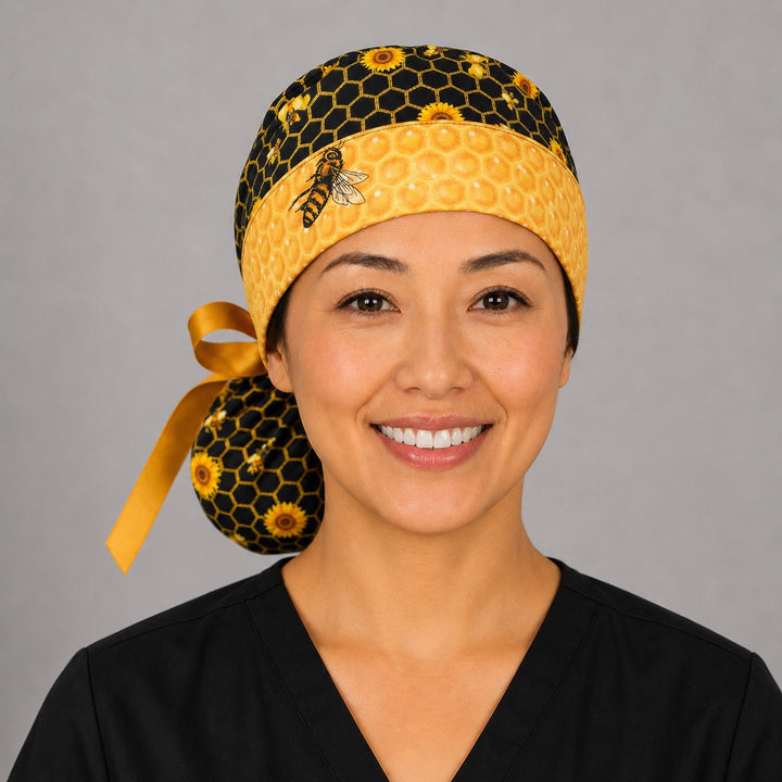 Smiling woman wearing honey bee and honeycomb ponytail scrub cap, front view showing sunflowers, bees, golden honeycomb band and gold ribbon tie