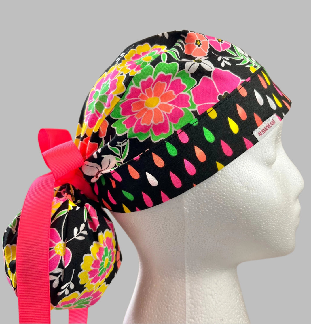 Neon floral ponytail scrub cap on mannequin, side profile showing gathered ponytail pouch and hot pink ribbon tie